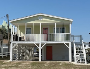 A two-story building with a balcony, a red door, and a white fence. - Cute Bungalow in Cherry Grove, SC. Just a Chip Shot from ocean & beach access! (North Myrtle Beach)