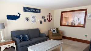 A living room with a sofa, armchair, coffee table, and wall decorations including a whale silhouette, anchor, and a sign that reads 'BEACH HOUSE'. - Cute Bungalow in Cherry Grove, SC. Just a Chip Shot from ocean & beach access! (North Myrtle Beach)