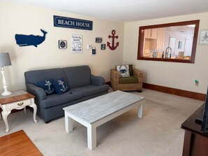 A living room with a sofa, armchair, coffee table, and wall decorations including a whale silhouette, anchor, and a sign that reads 'BEACH HOUSE'. - Cute Bungalow in Cherry Grove, SC. Just a Chip Shot from ocean & beach access! (North Myrtle Beach)