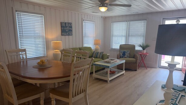 A dining area with a wooden table and chairs, a green sofa, a small coffee table, and a ceiling fan. - Cute Bungalow in Cherry Grove, SC. Just a Chip Shot from ocean & beach access! (North Myrtle Beach)
