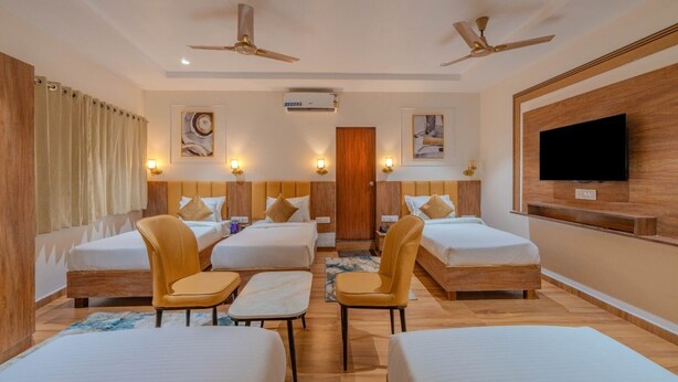 Une chambre d’hôtel avec deux lits simples, deux fauteuils, une télévision, des ventilateurs de plafond et des œuvres d’art accrochées aux murs.