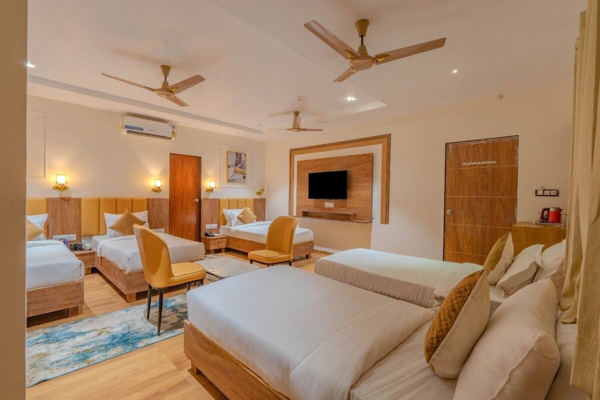 A hotel room with two beds, a TV, ceiling fans, and a wooden wardrobe.