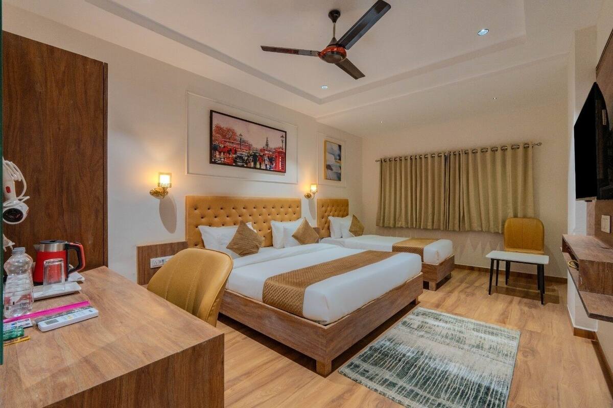 A hotel room with a large bed, two bedside tables, a desk, a chair, a ceiling fan, and a TV.
