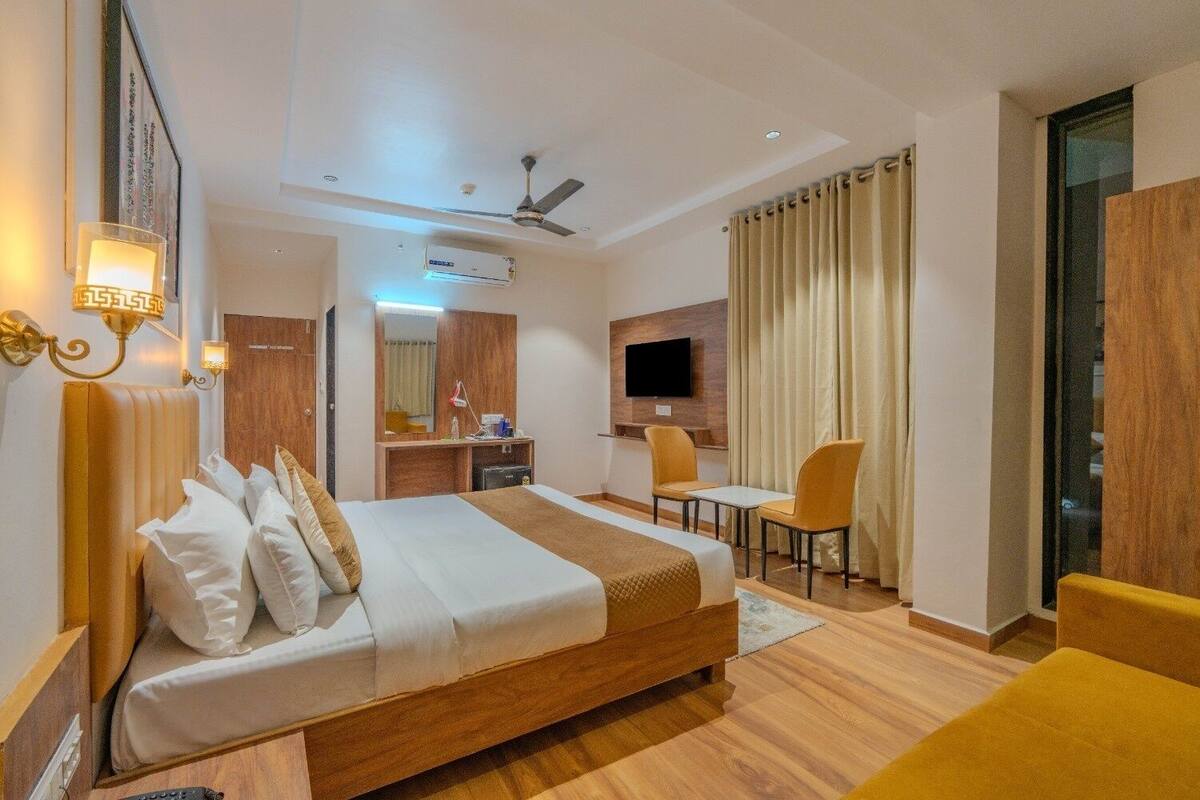 A hotel room with a large bed, a desk with a chair, a television, and a ceiling fan.