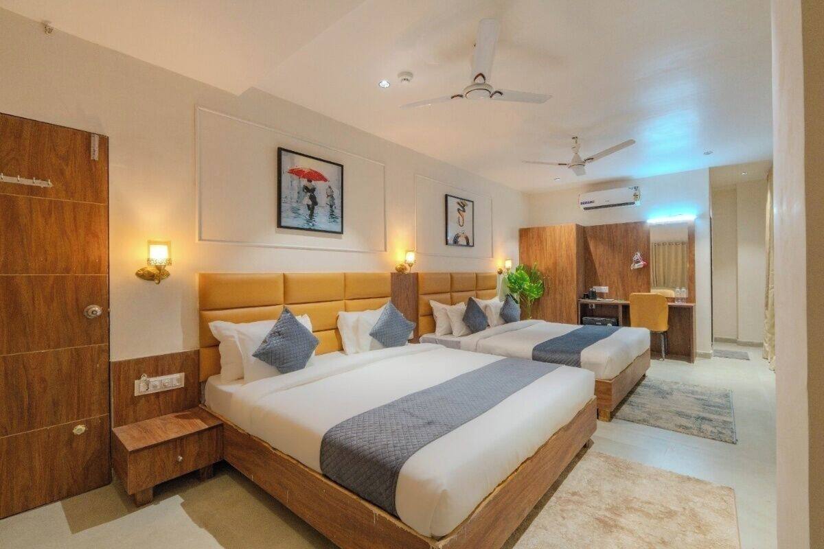 A hotel room with two beds, wooden headboards, wall-mounted lights, and a ceiling fan.
