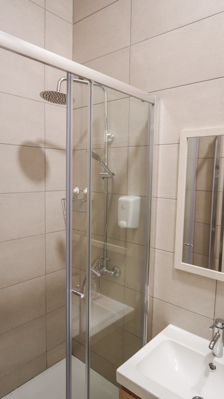 A glass-enclosed shower with a handheld showerhead and a wall-mounted soap dispenser.