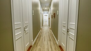 Egy folyosó, fehér ajtókkal, fa parkettával és világos színű falakkal.