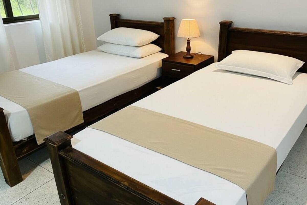 A hotel room with two single beds, a nightstand with a lamp, and a window with curtains.