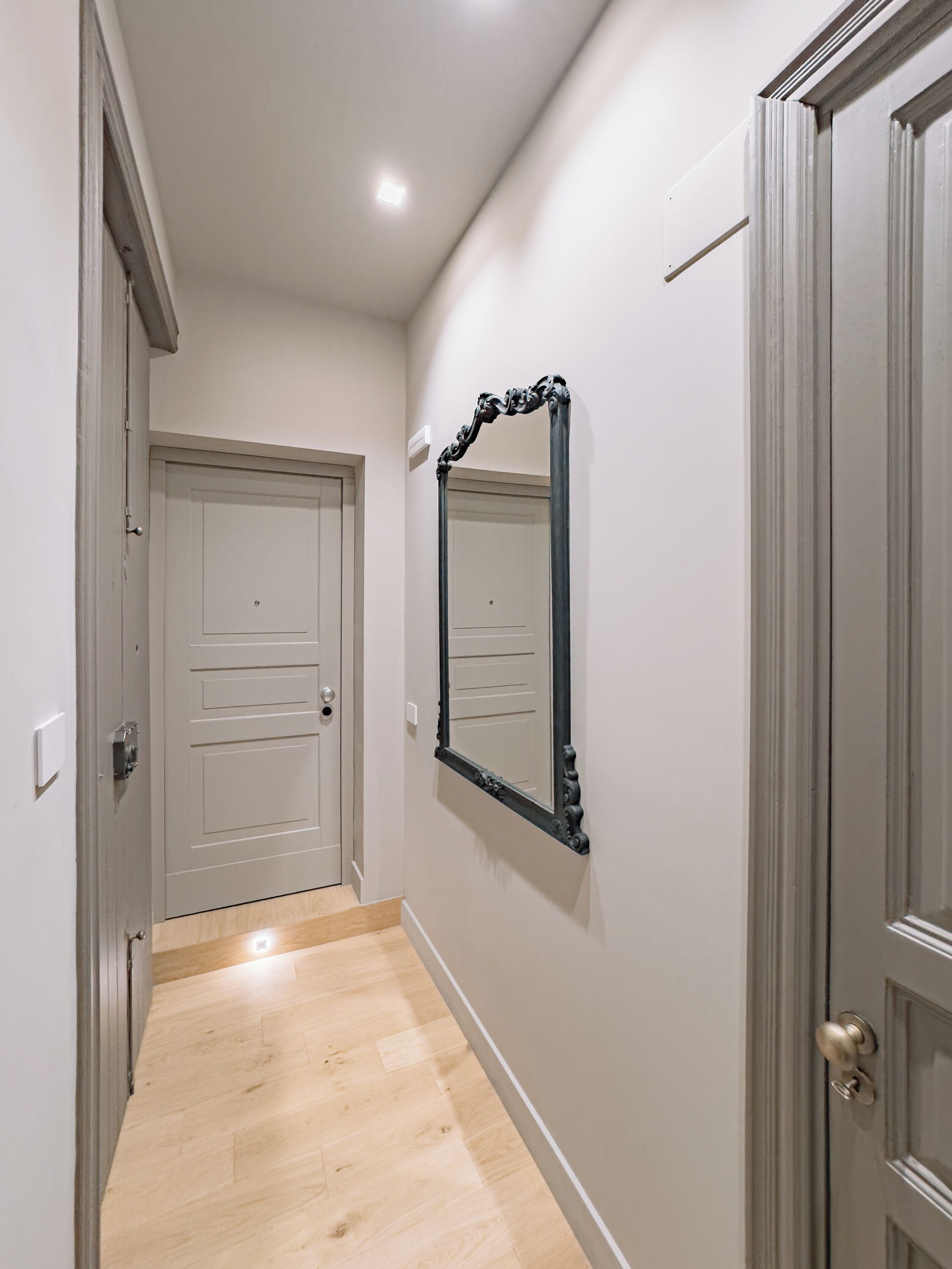 Un pasillo con piso de madera, una puerta blanca y un espejo en la pared.