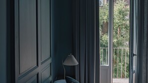 Ein Schlafzimmer mit einem großen Bett, einer Nachttischlampe und Blick auf einen Balkon mit Vorhängen.