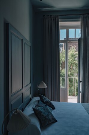 A bedroom with a large bed, a bedside lamp, and a view of a balcony with curtains. - Silva Apartment (Catania)