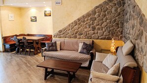 A cozy living area with a stone accent wall, a wooden dining table, and a sofa with cushions. - Gran Paradis Aprica - Casa Giulia (Corteno Golgi)