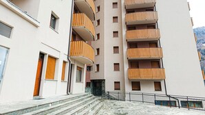 A multi-story residential building with balconies, a staircase leading to the entrance, and a paved ground area. - Gran Paradis Aprica - Casa Giulia (Corteno Golgi)