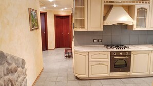 A kitchen with a built-in gas stove, oven, and white cabinetry. There is a stone accent wall and a framed picture on the left. - Gran Paradis Aprica - Casa Giulia (Corteno Golgi)