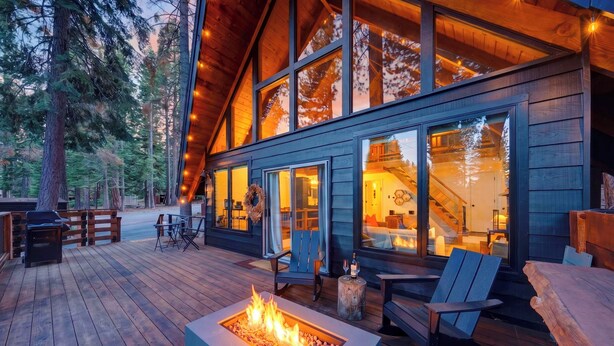 A wooden deck with a fire pit, outdoor seating, and a large windowed building. - Modern Cabin • Spa • Firepit & Deck • Near Palisades | Tahoe A-Frame Retreat (Carnelian Bay)
