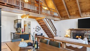 A spacious kitchen with a dining area, a fireplace, and a staircase leading to an upper level. - Modern Cabin • Spa • Firepit & Deck • Near Palisades | Tahoe A-Frame Retreat (Carnelian Bay)