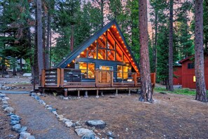 A cabin with a sloped roof, large windows, and a deck. - Modern Cabin • Spa • Firepit & Deck • Near Palisades | Tahoe A-Frame Retreat (Carnelian Bay)