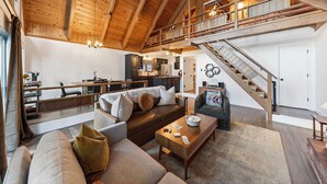 A spacious living area with a high ceiling, wooden beams, a staircase, and a cozy seating arrangement. - Modern Cabin • Spa • Firepit & Deck • Near Palisades | Tahoe A-Frame Retreat (Carnelian Bay)