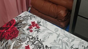 Ein Bett mit einem blumigen Überwurf, ein Stapel brauner Kissen und ein pinkfarbener Vorhang in einem Schlafzimmer.