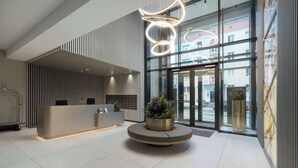 Ett modernt entréområde med en receptionsdisk, en rund plantering med växter och en stor glasingång.
