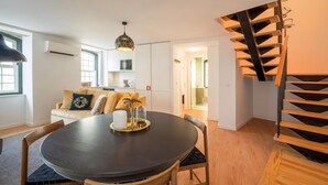 Une cuisine moderne avec des meubles blancs, un coin repas doté d’une table ronde et un escalier avec des marches en bois.
