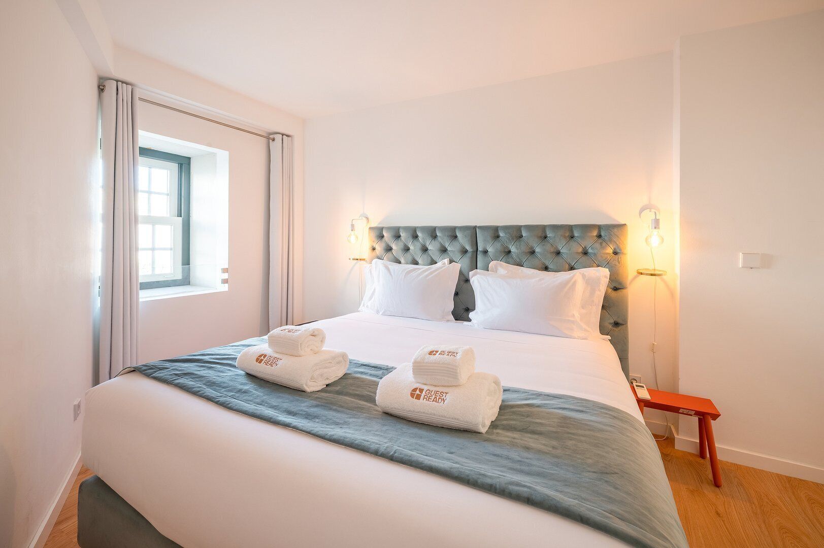 A hotel room with a large bed, two pillows, a headboard, and two wall-mounted lamps.