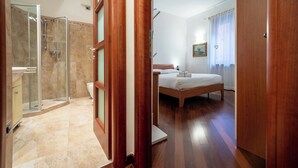 A hotel room with a wooden floor, a bed, a shower area, and a bathroom. - Elegant Apartment 300 Meters from the Arena with balcony (Verona)