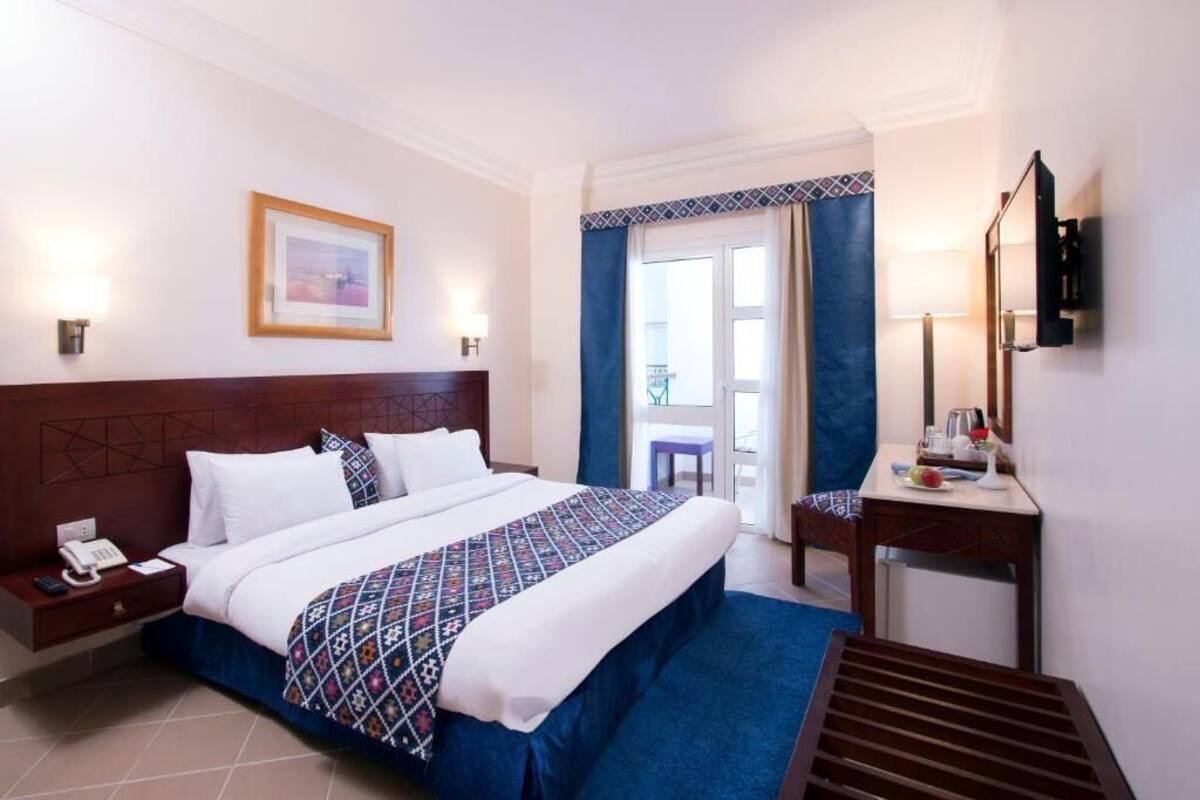 A hotel room with a large bed, a bedside table with a phone, a small table with a lamp, and a TV mounted on the wall.