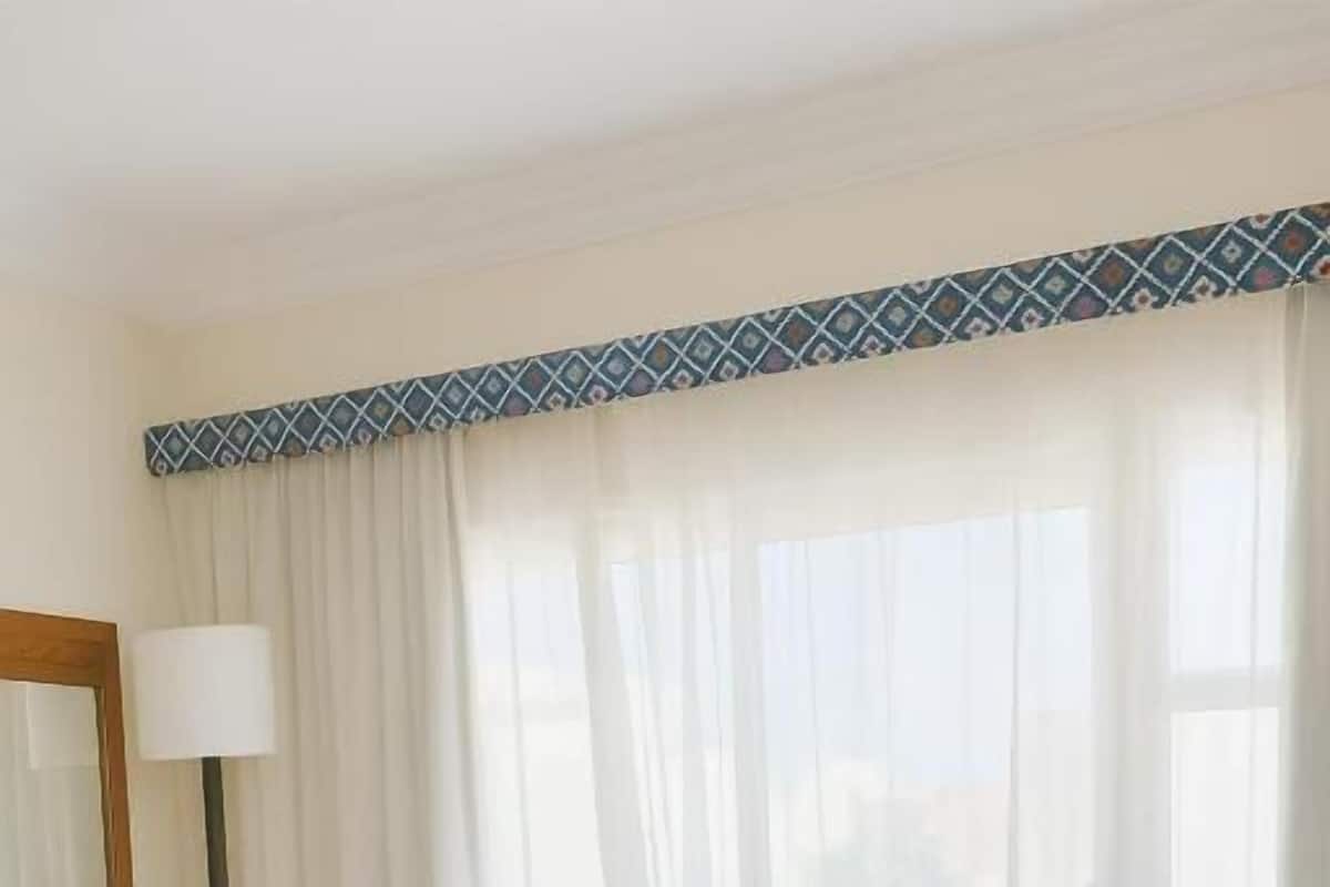 A hotel room with a bed, a desk with a lamp, and a window with sheer curtains.