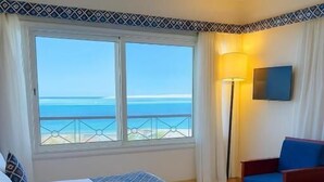 Een hotelkamer met een bed, een stoel, een bureau, een televisie en uitzicht op de oceaan.