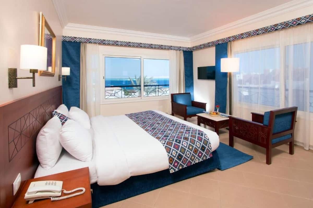 A hotel room with a large bed, a desk, a chair, and a view of the sea.