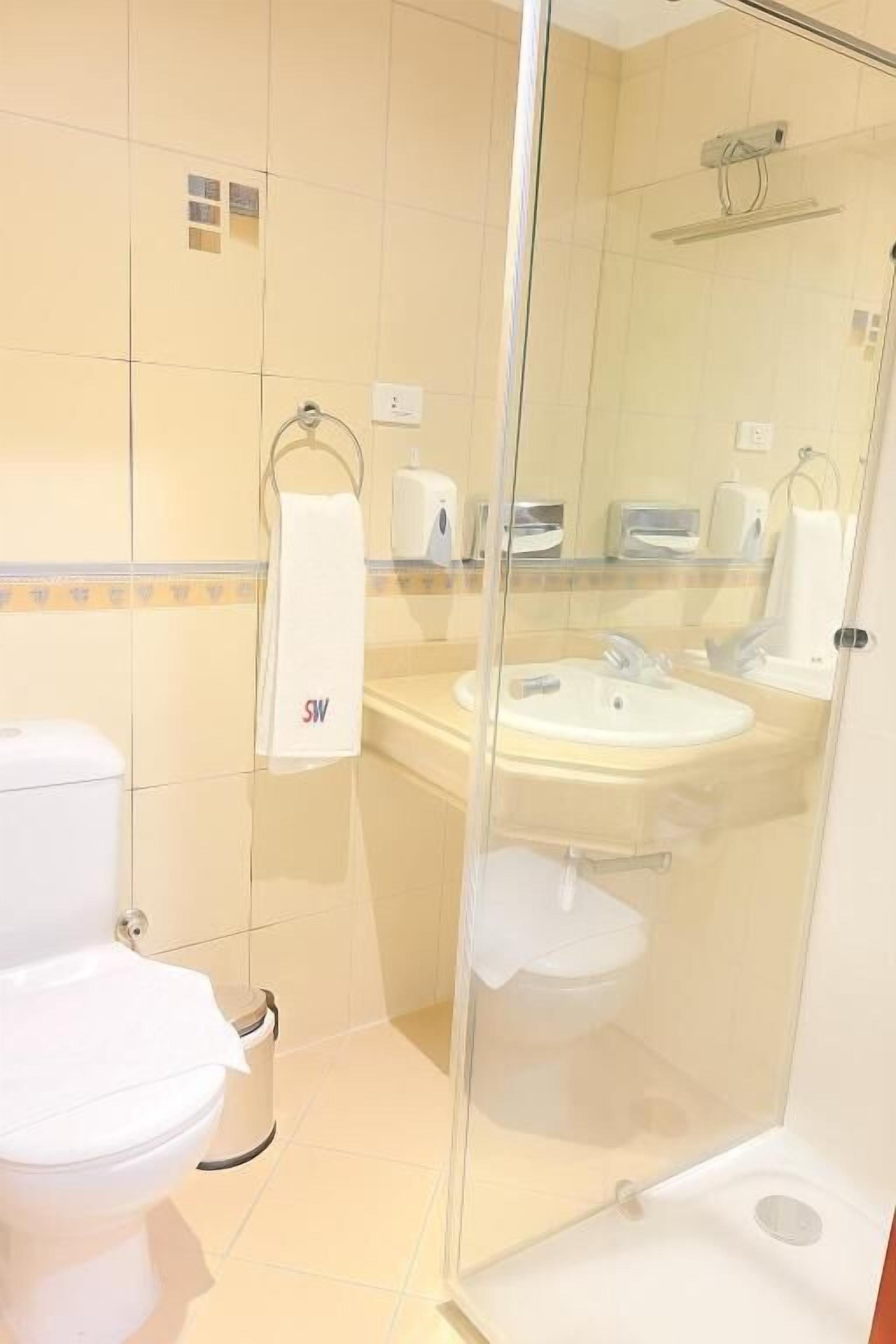 A bathroom with a toilet, sink, and glass shower enclosure.