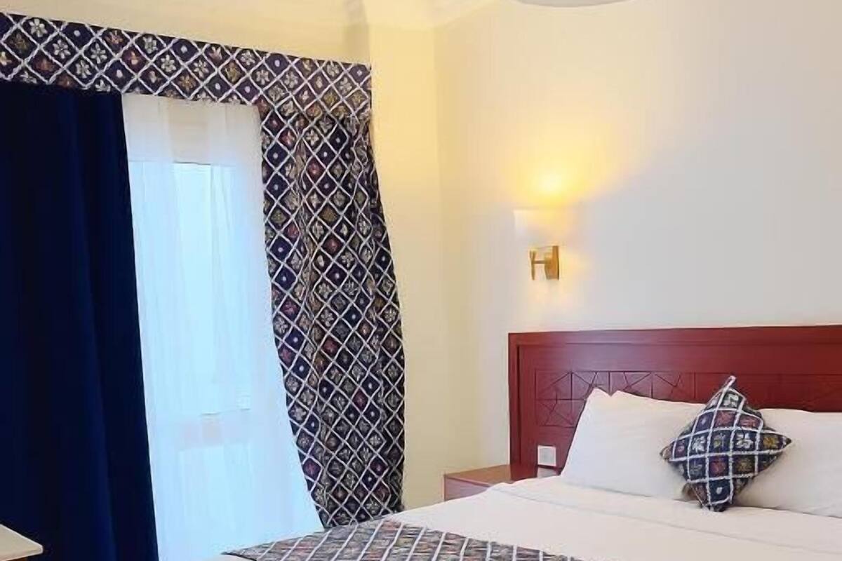 A hotel room with a large bed, a nightstand, a lamp, and a window with curtains.