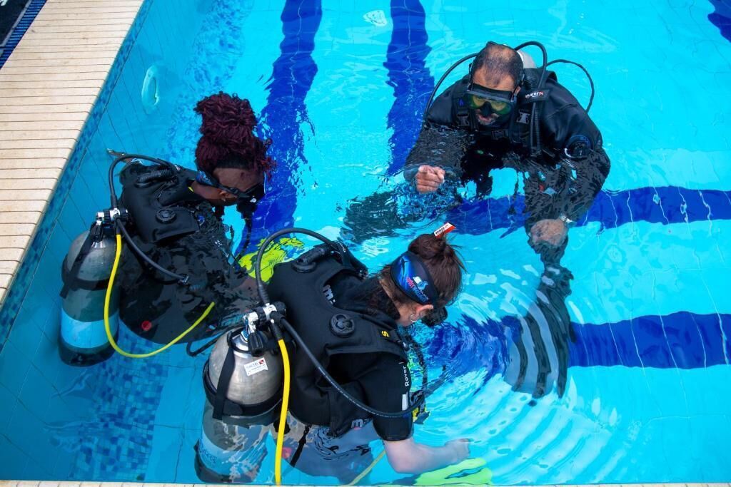 Una piscina con tres buzos equipados.