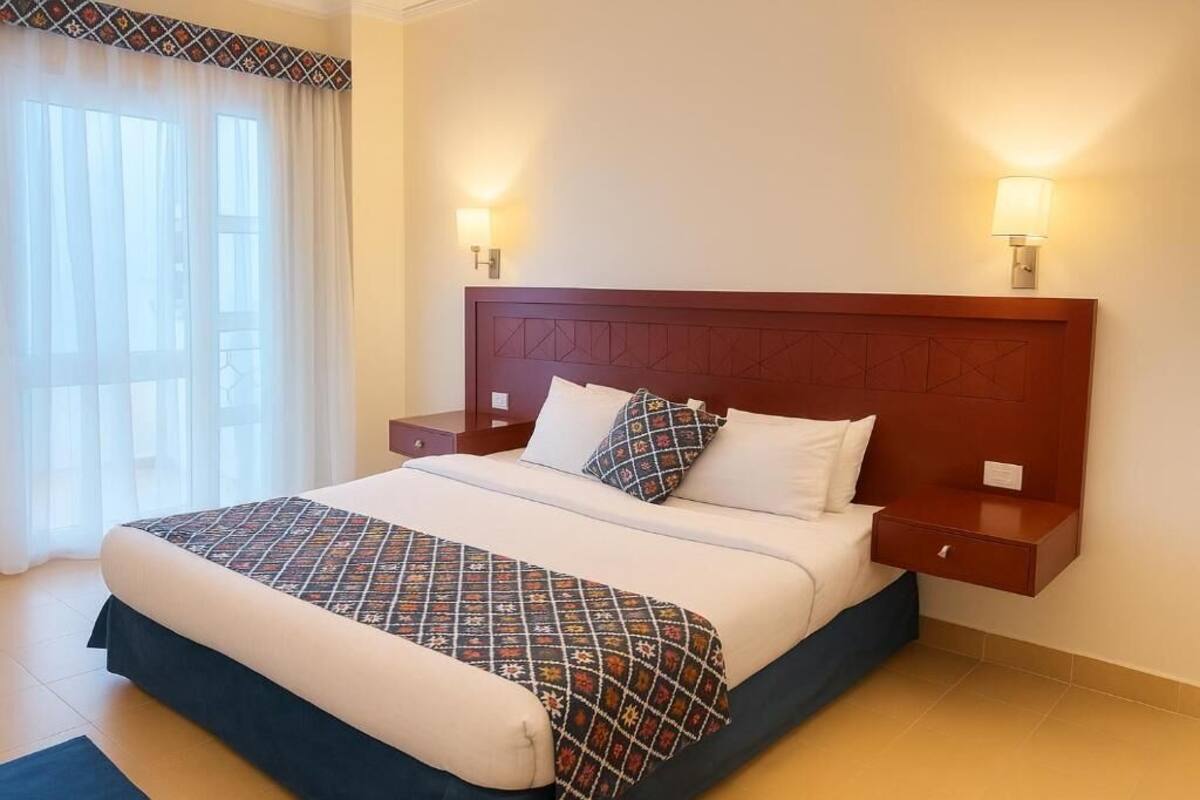 A neatly made bed with a patterned bedspread, two bedside lamps, and a nightstand with a drawer.