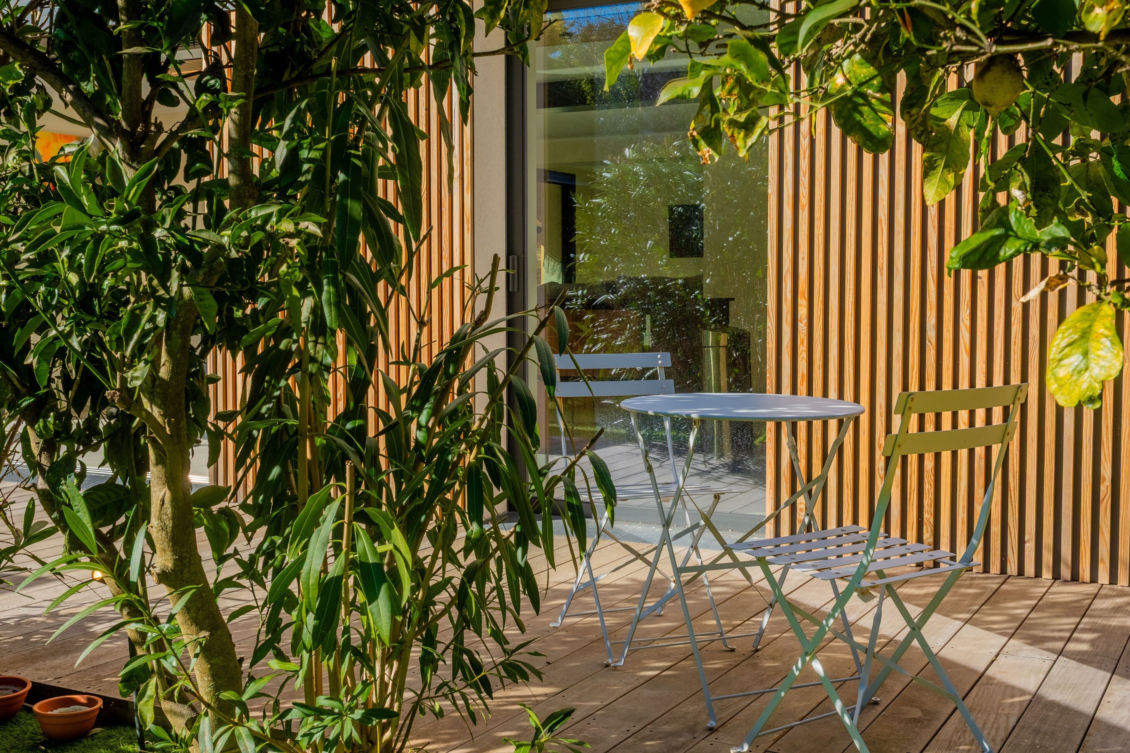 Une terrasse extérieure avec une table et des chaises, entourée de verdure et d’une clôture en bois.