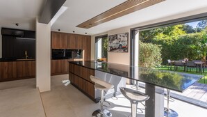 A modern kitchen with a glass island, wooden cabinets, and a view of a garden.