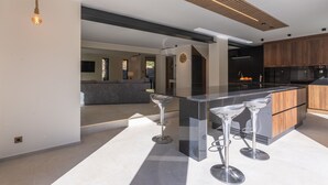 A modern kitchen with a central island, bar stools, and a hanging light fixture.
