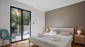 A bedroom with a large bed, a chair, a nightstand, and a view through a sliding door.