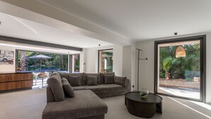 A modern living room with a sectional sofa, a round coffee table, and large windows offering a view of the outdoors.