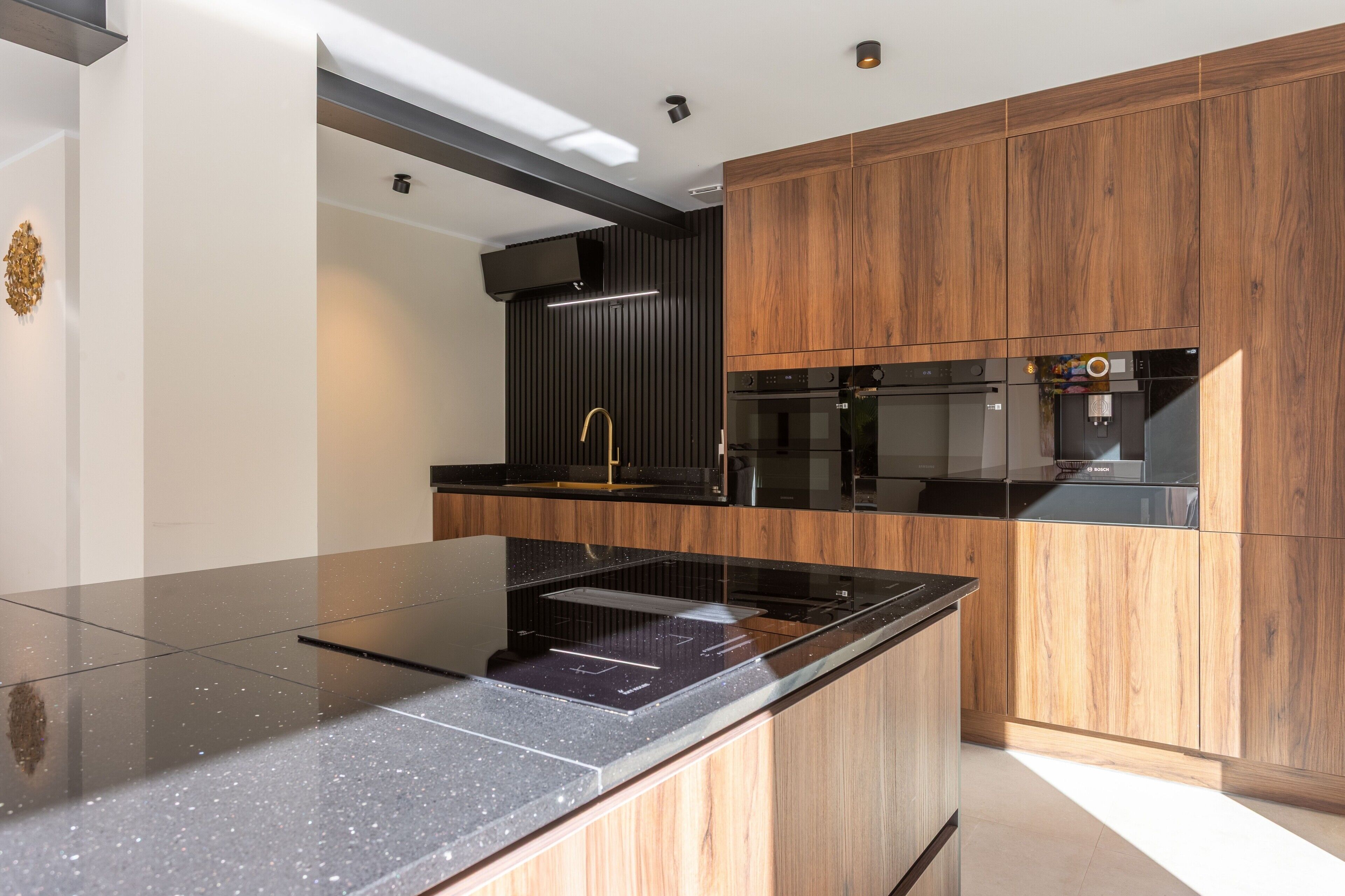 Una cocina moderna con encimera negra, armarios de madera y electrodomésticos integrados.