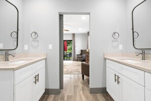 A modern bathroom with two sinks, a walk-in shower, and a view into a living area with a dining table and chairs. - Newly Constructed Home near Downtown and Beaches (West Palm Beach)