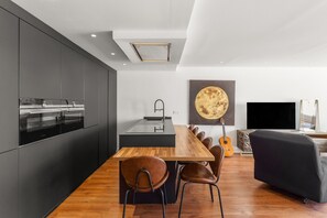 A modern kitchen with a built-in oven, a dining area with a wooden table and chairs, a black sofa, and a large painting on the wall. - Duplex 'Paradise Over the Sea' with Sea Views, Wi-Fi and Air Conditioning (Benalmádena)