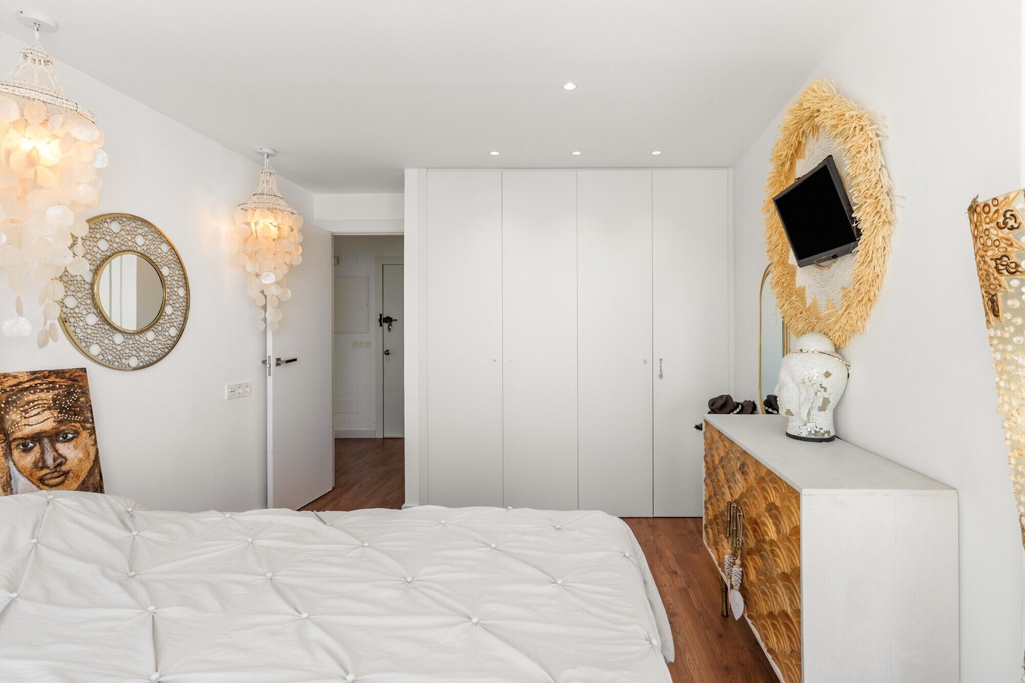 A bedroom with a bed, a dresser, a mirror, a chandelier, and a television.