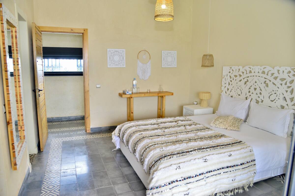 A bedroom with a bed, bedside table, lamp, and wall decorations.