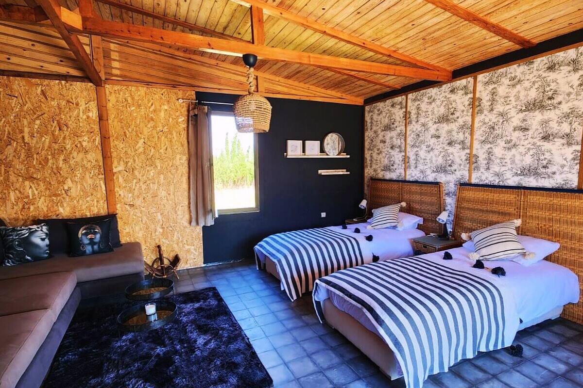 A room with two beds, a sofa, a small table with a candle, and a black rug.