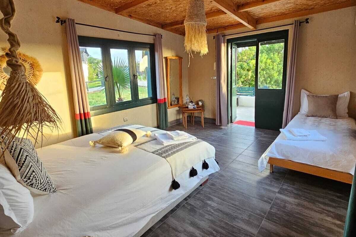 A room with a bed, a chair, a hanging light fixture, and a view through a window.