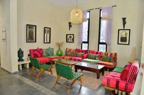 A living room with colorful sofas, a green chair, a table, and a hanging light fixture. - Meezane Farmhouse (Bir Jdid)