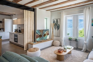 Ein modernes Wohnzimmer mit großem Fernseher, einem Holztisch und Meerblick durch große Fenster.