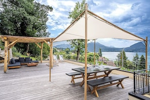 Eine Holzterrasse mit Tisch und Bänken, einer Sitzecke und einer Pergola mit Dach.
